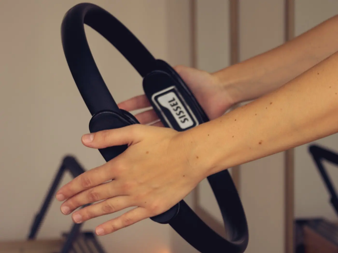 Dłonie trzymające ring do pilatesu, w tle reformer